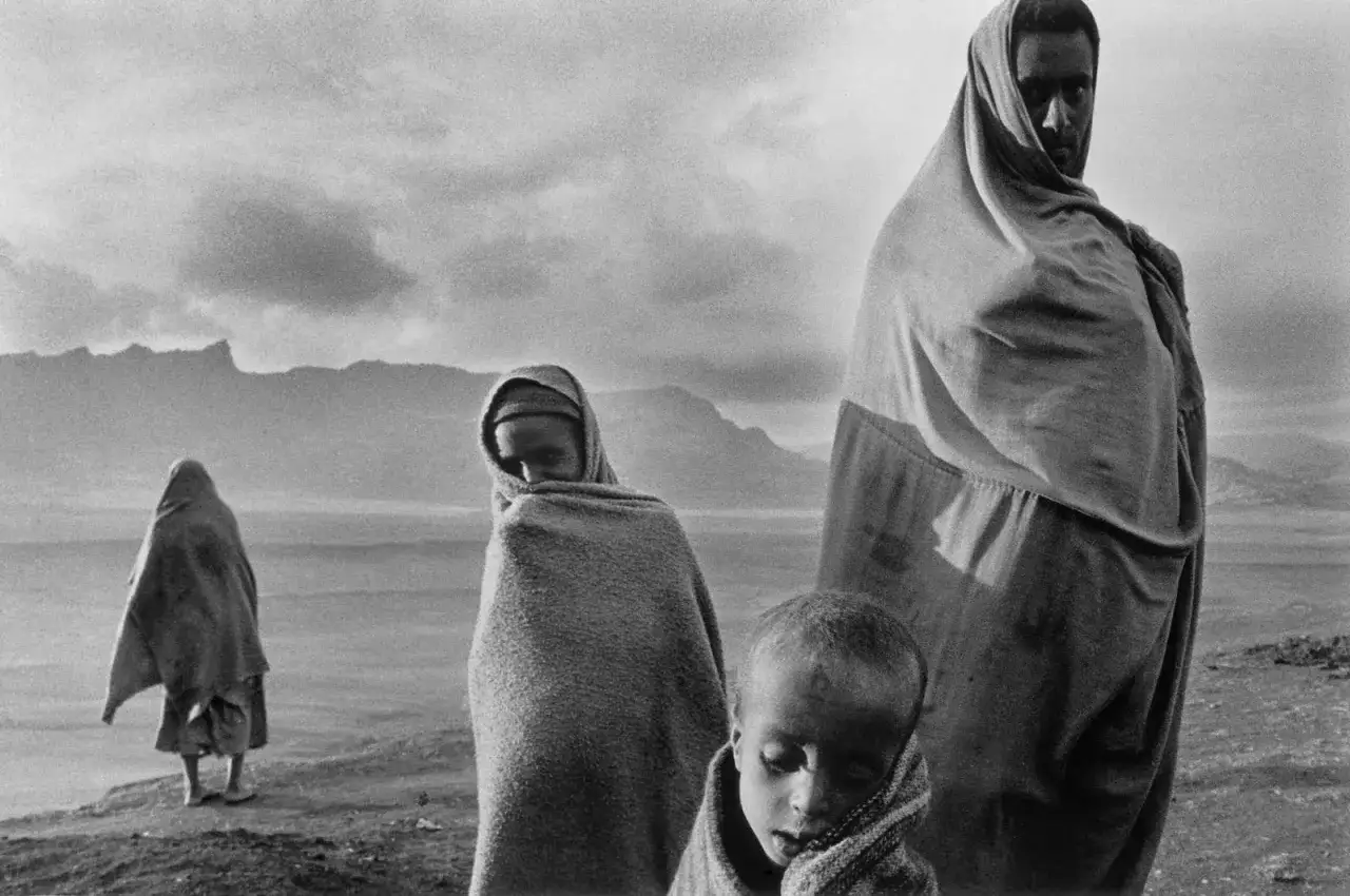 Sebastião Salgado cattura la resilienza di una famiglia avvolta in coperte, con montagne sullo sfondo.