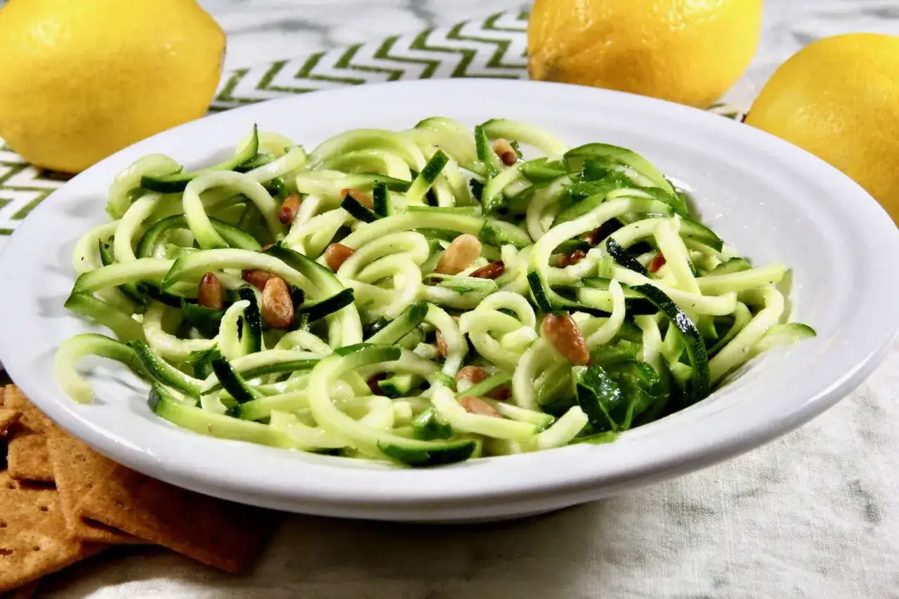 Un plat de tagliatelles de courgettes fra&icirc;ches, garni de pignons de pin, avec des citrons en arri&egrave;re-plan.
