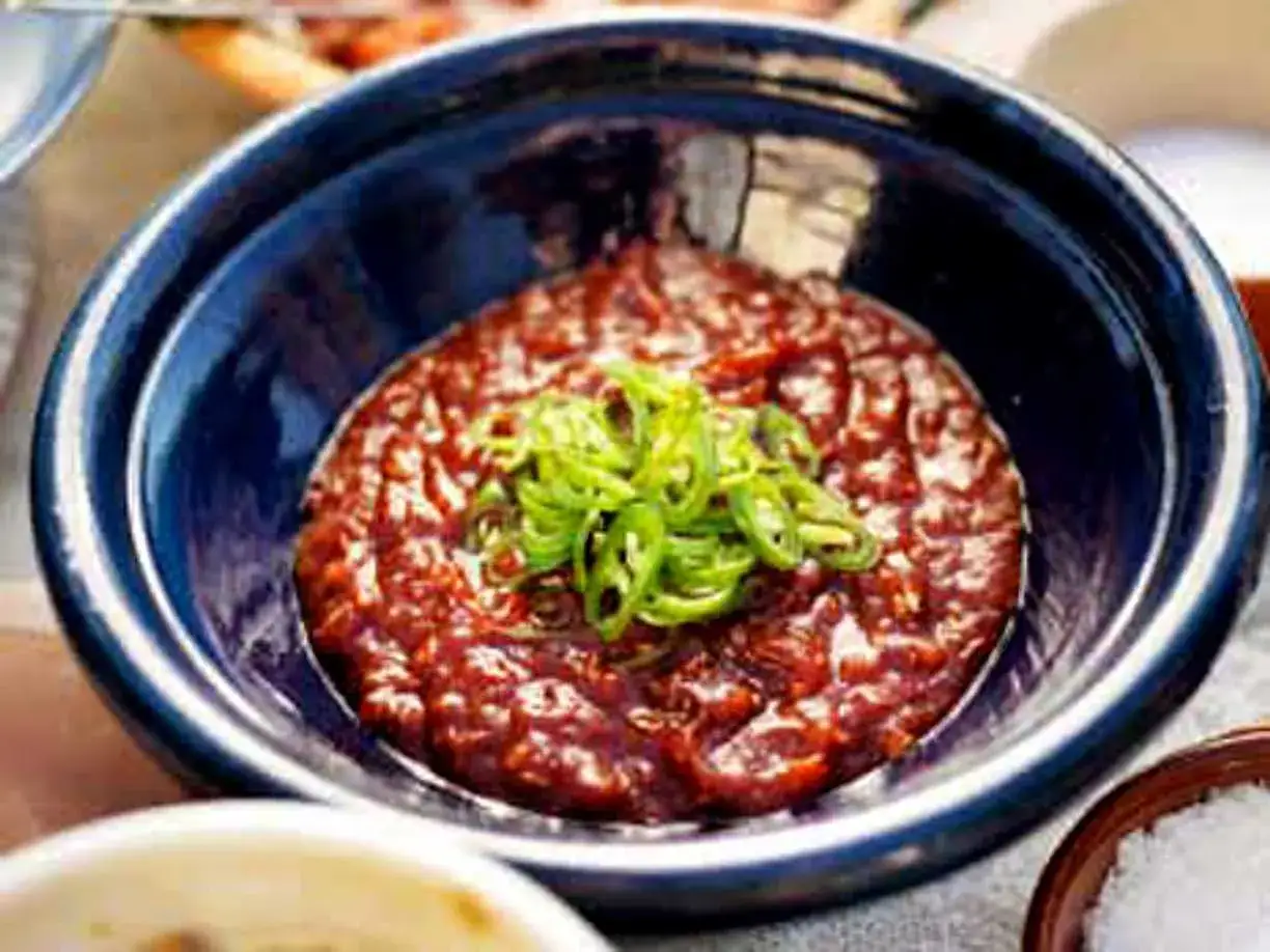 En skål med mörk, kryddig bbq sås toppad med strimlad grön chili. Perfekt för grillkvällen!