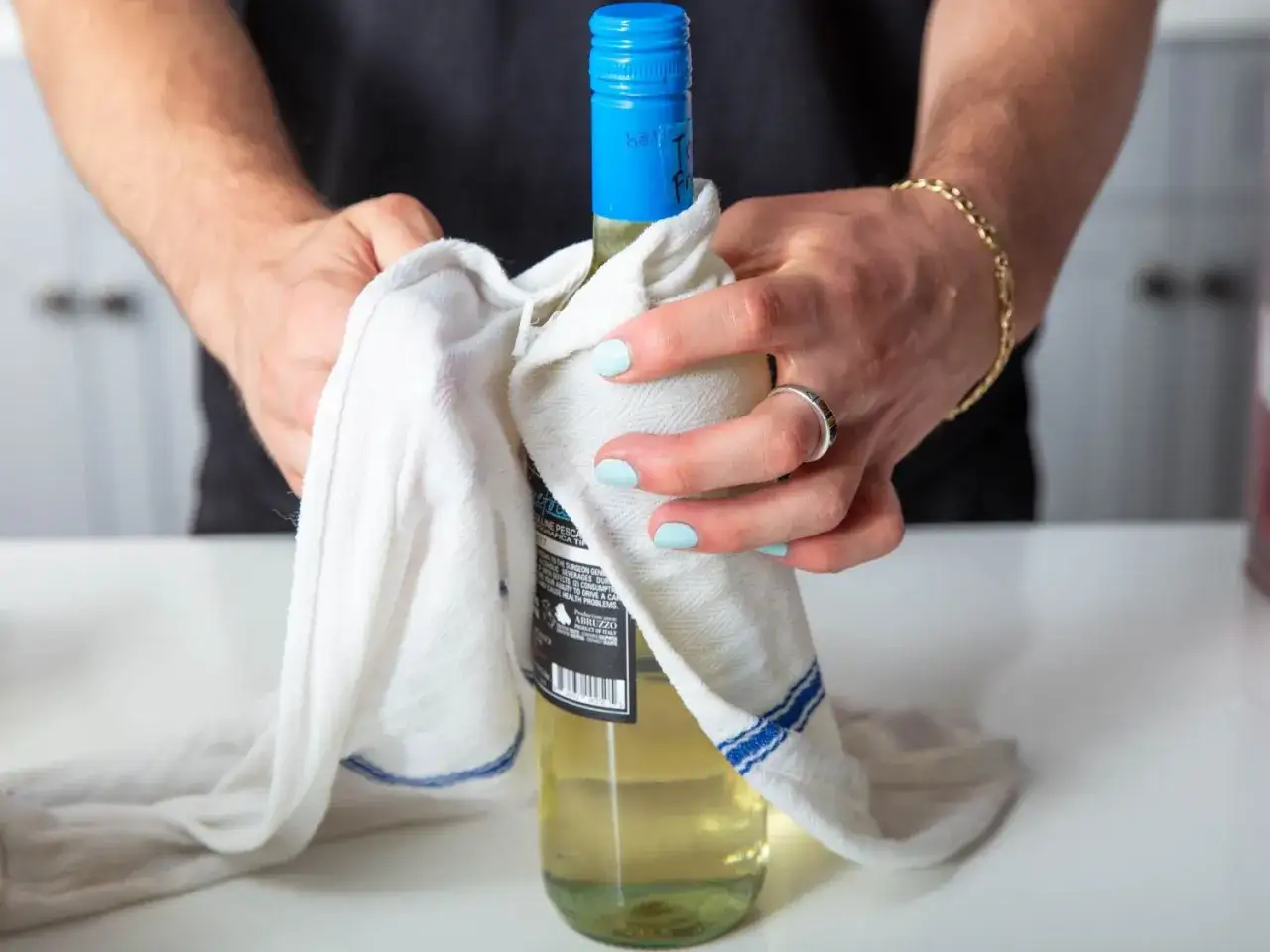 Mani che asciugano una bottiglia di vino bianco con un panno. Quanto tempo pu&ograve; stare il vino bianco in freezer?