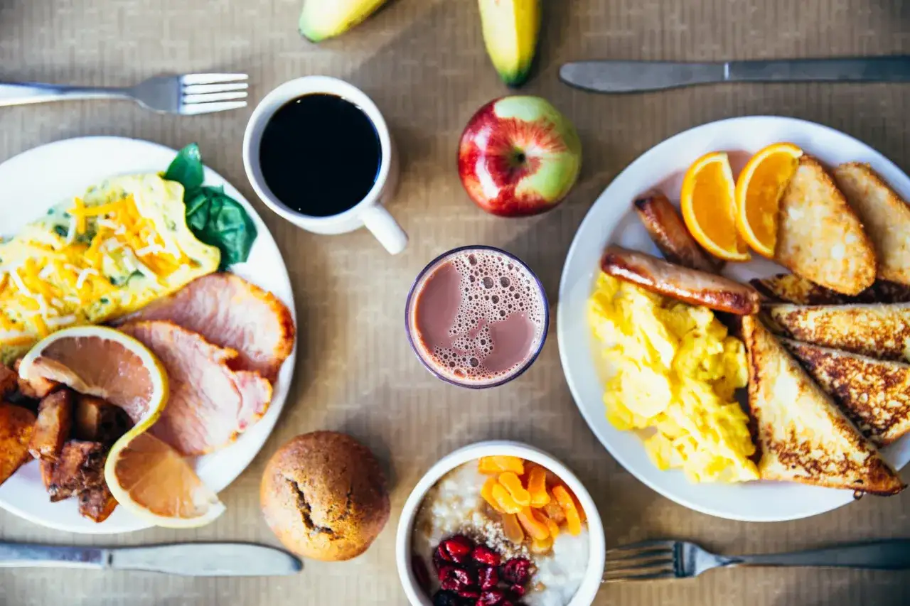 Un petit déjeuner prise de masse copieux avec œufs brouillés, bacon, toasts, saucisses, fruits et café.