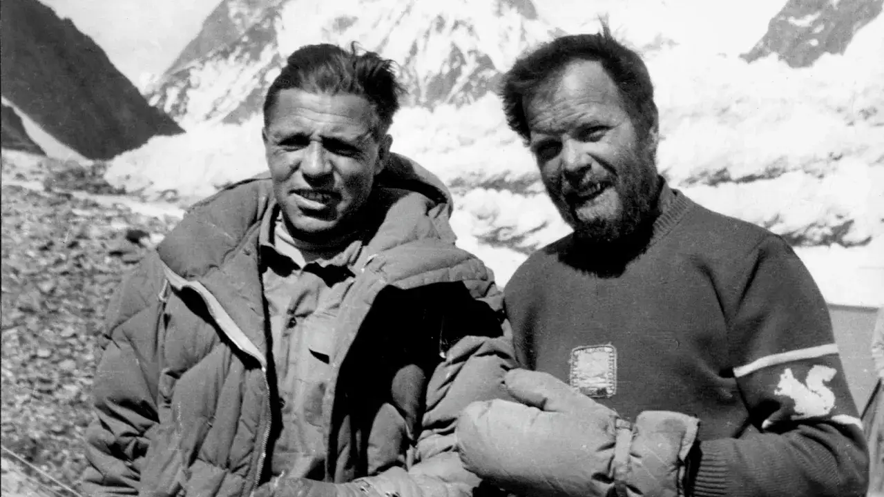 Zwei Bergsteiger nach der K2 Erstbesteigung. Sie l&auml;cheln ersch&ouml;pft, aber gl&uuml;cklich vor schneebedeckten Gipfeln.