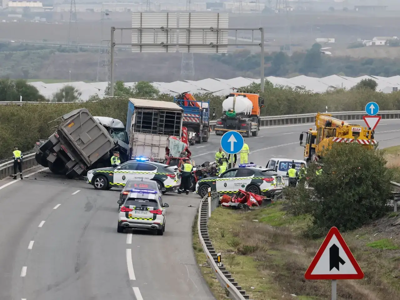 Accidente múltiple en la autopista con camiones volcados y coches de la Guardia Civil. Equipos de emergencias trabajan en la zona.