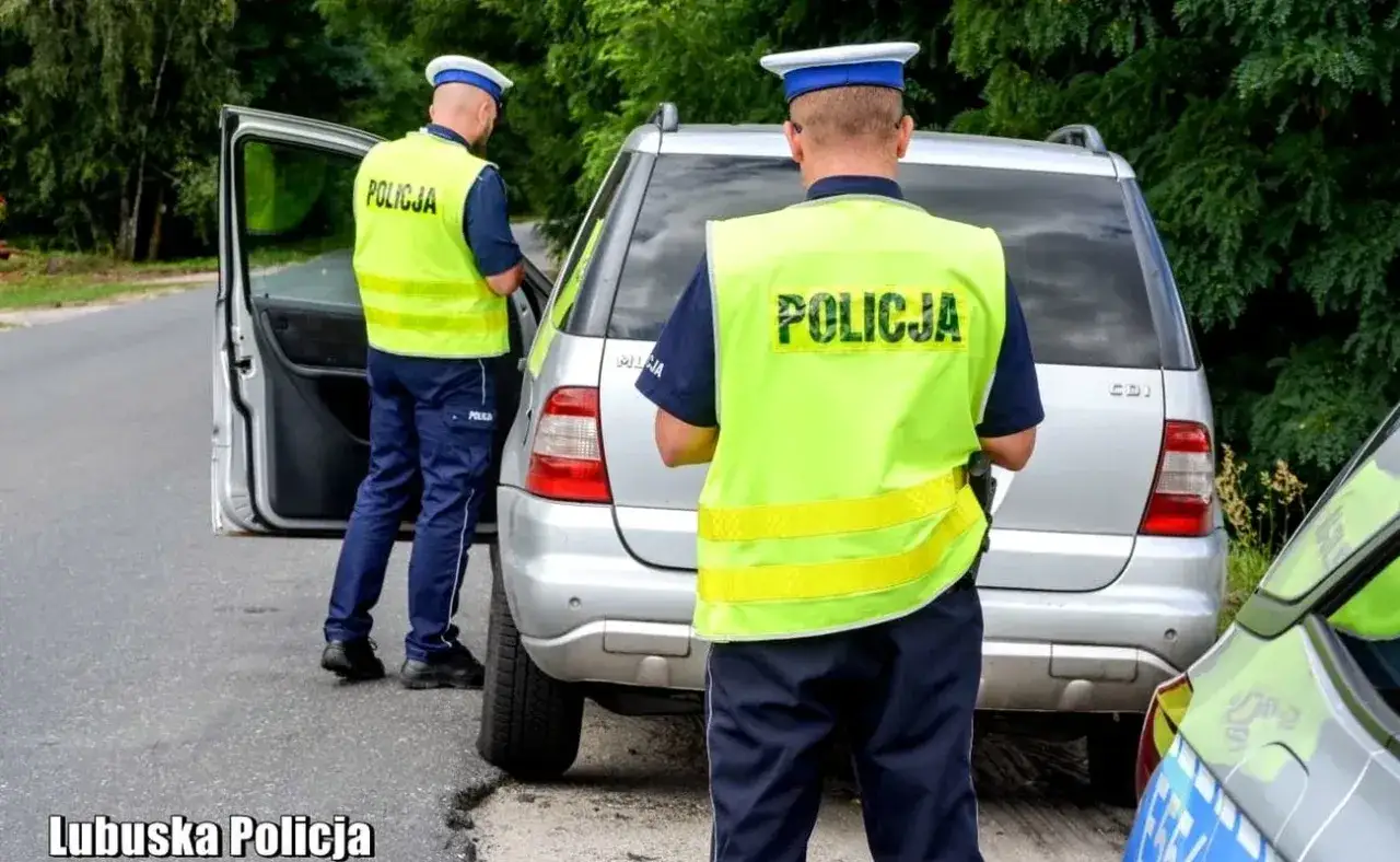Dwóch policjantów w kamizelkach odblaskowych przy srebrnym samochodzie. Jeden z nich otwiera drzwi. Sytuacja może być związana z niezatrzymaniem się do kontroli.