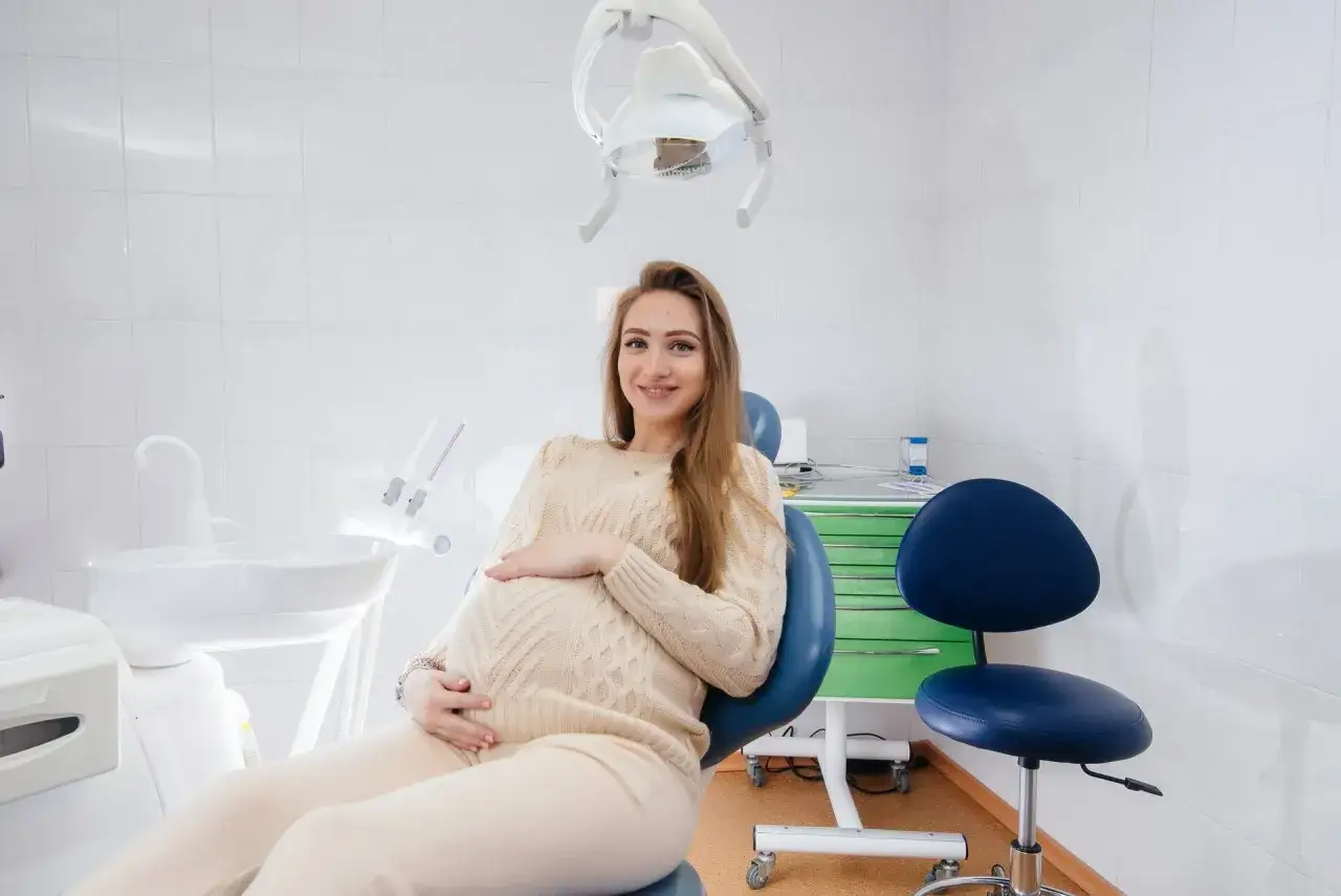 Uśmiechnięta ciężarna kobieta siedzi na fotelu dentystycznym, czując się komfortowo z znieczuleniem u dentysty w ciąży.
