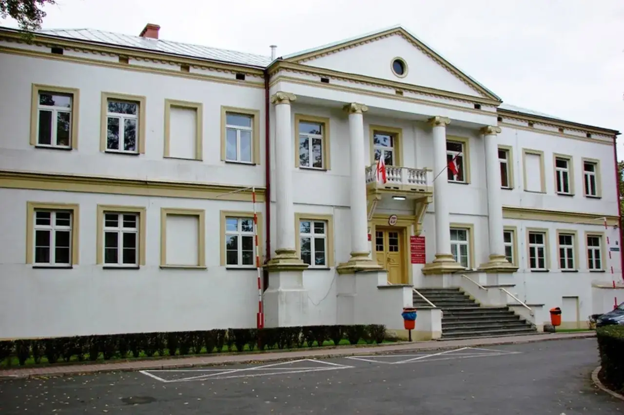 Biały budynek z kolumnami i balkonem, przypominający zamek w Wieluniu.