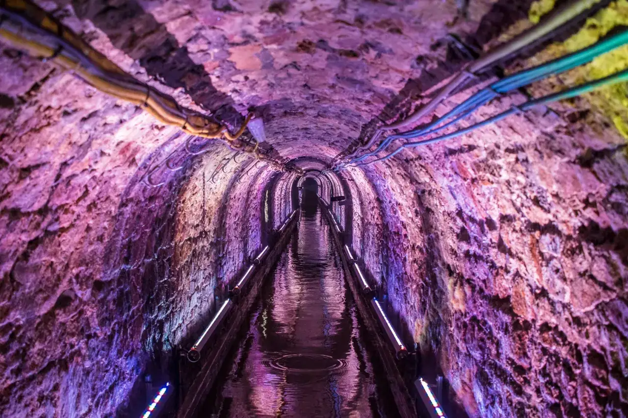 Podziemny tunel z kamienia, oświetlony fioletowym światłem, z wodą na dnie. Idealne miejsce, gdzie jechać w niedzielę na Śląsku, by poczuć klimat dawnych kopalń.