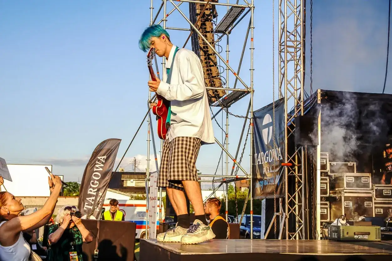 Artysta z niebieskimi włosami gra na gitarze na scenie. Tribbs wzrost robi wrażenie na widzach, którzy robią zdjęcia.