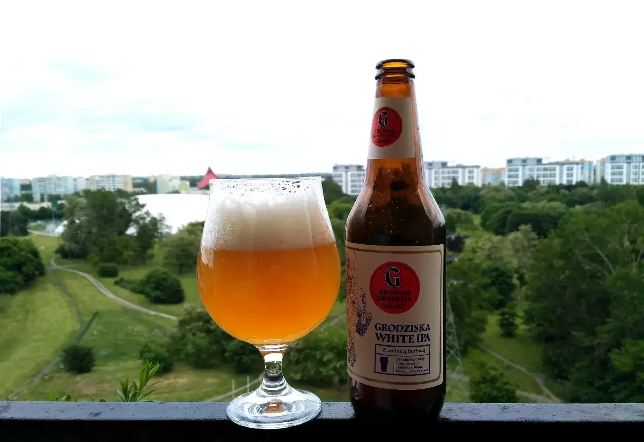 Grodziska White IPA w szkle i butelce, z widokiem na zieleń i miasto. Idealne na letni wiecz&oacute;r.