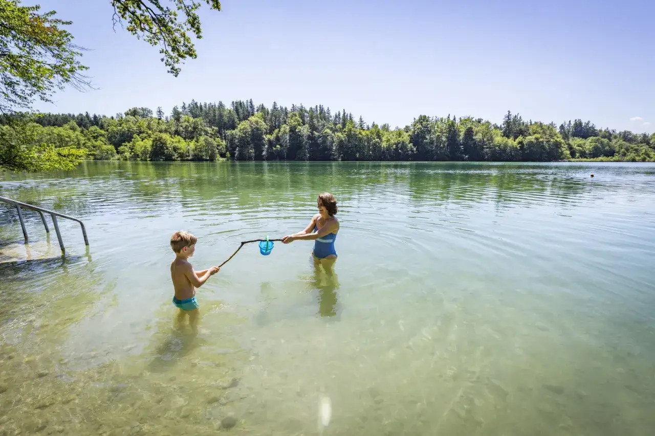 Mutter und Sohn spielen im See zum Schwimmen. Sie halten einen Stock mit einem blauen Eimer, um etwas zu fangen.