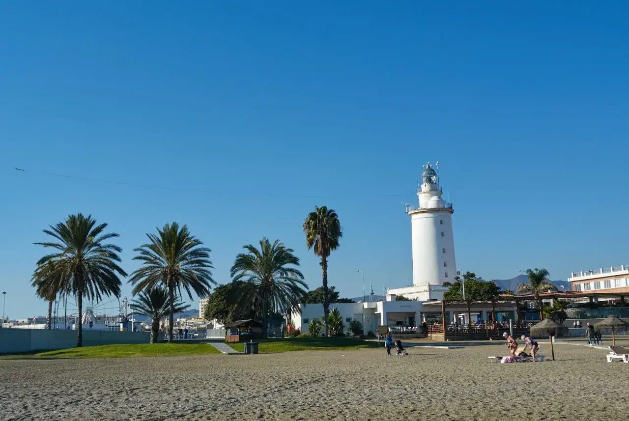 Malaga pogoda listopad: słoneczny dzień na plaży z palmami i latarnią morską.