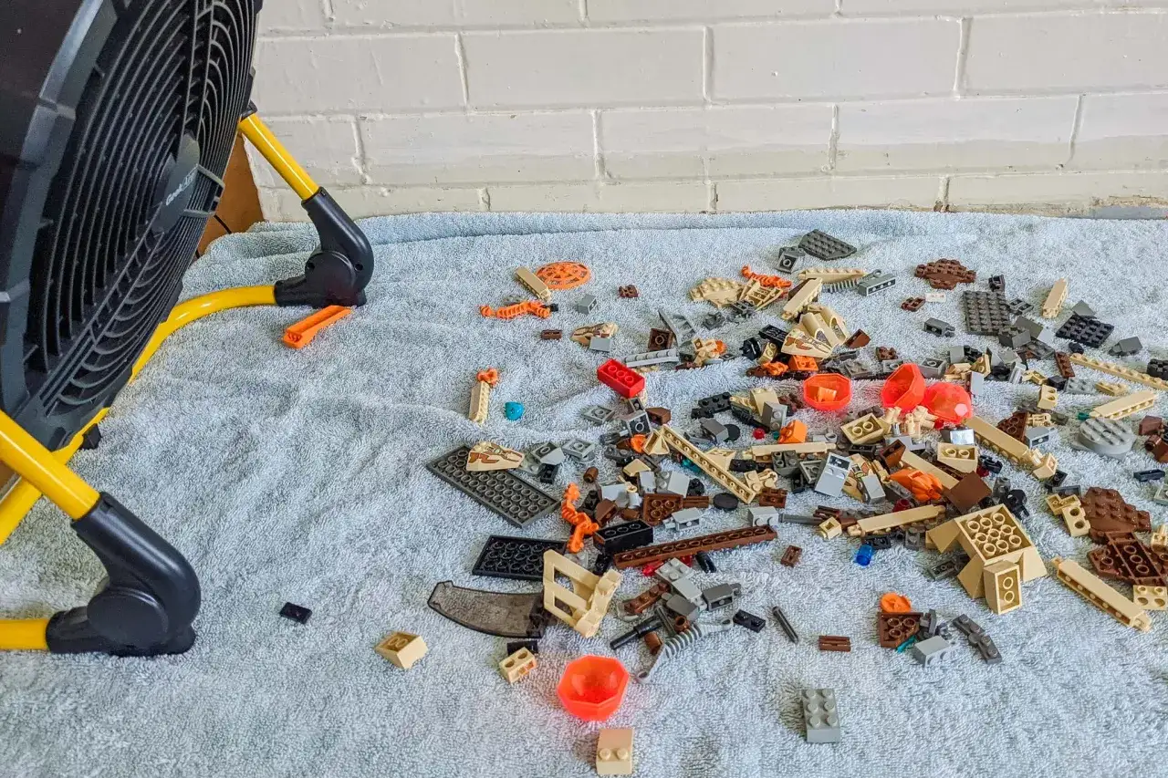 Ein Ventilator hilft beim Lego entstauben. Verstreute Bausteine liegen auf einer weichen Unterlage.