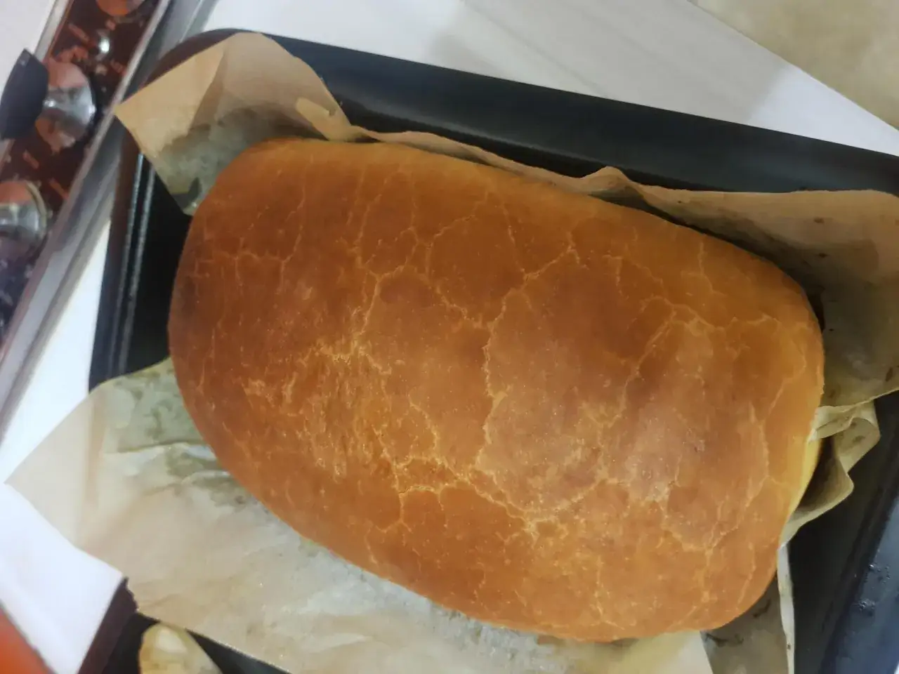 Ein goldbraunes Brot mit knuspriger Kruste liegt auf Backpapier. Perfekt zum **brot ohne risse backen**.