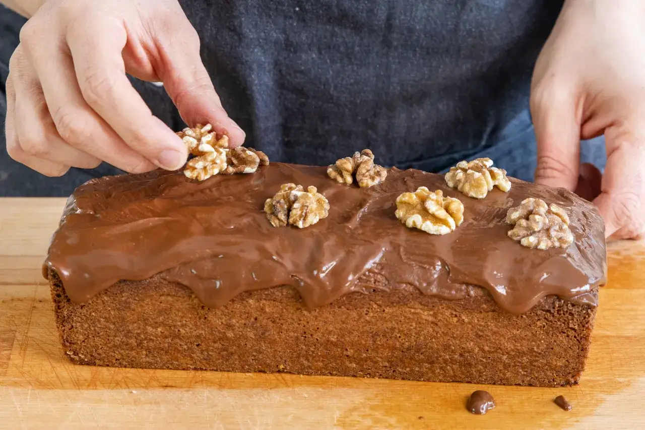 Hände garnieren einen Schokoladenkuchen mit Walnüssen. Dieser beste Walnusskuchen sieht köstlich aus!