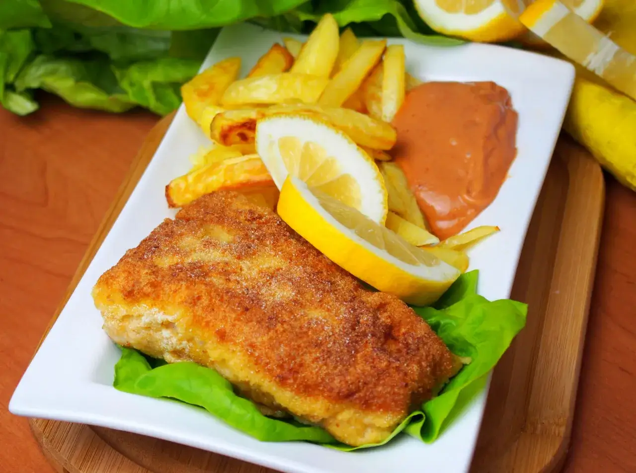 Pyszne Fish and Chips przepis: chrupiąca ryba w panierce, złociste frytki, sos i cytryna na białym talerzu.