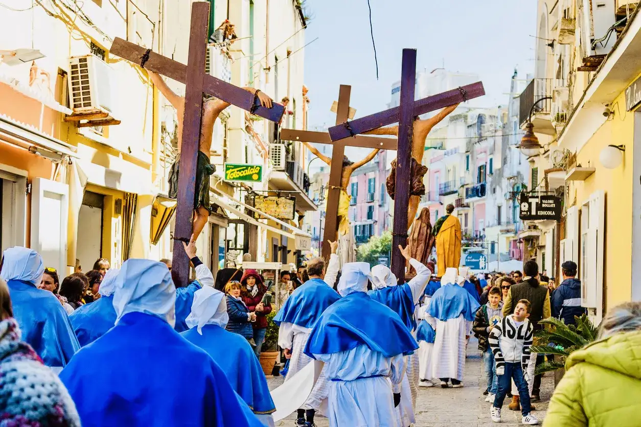 A solemn procession during Holy Week in Italy, with participants carrying crosses and figures of Jesus.