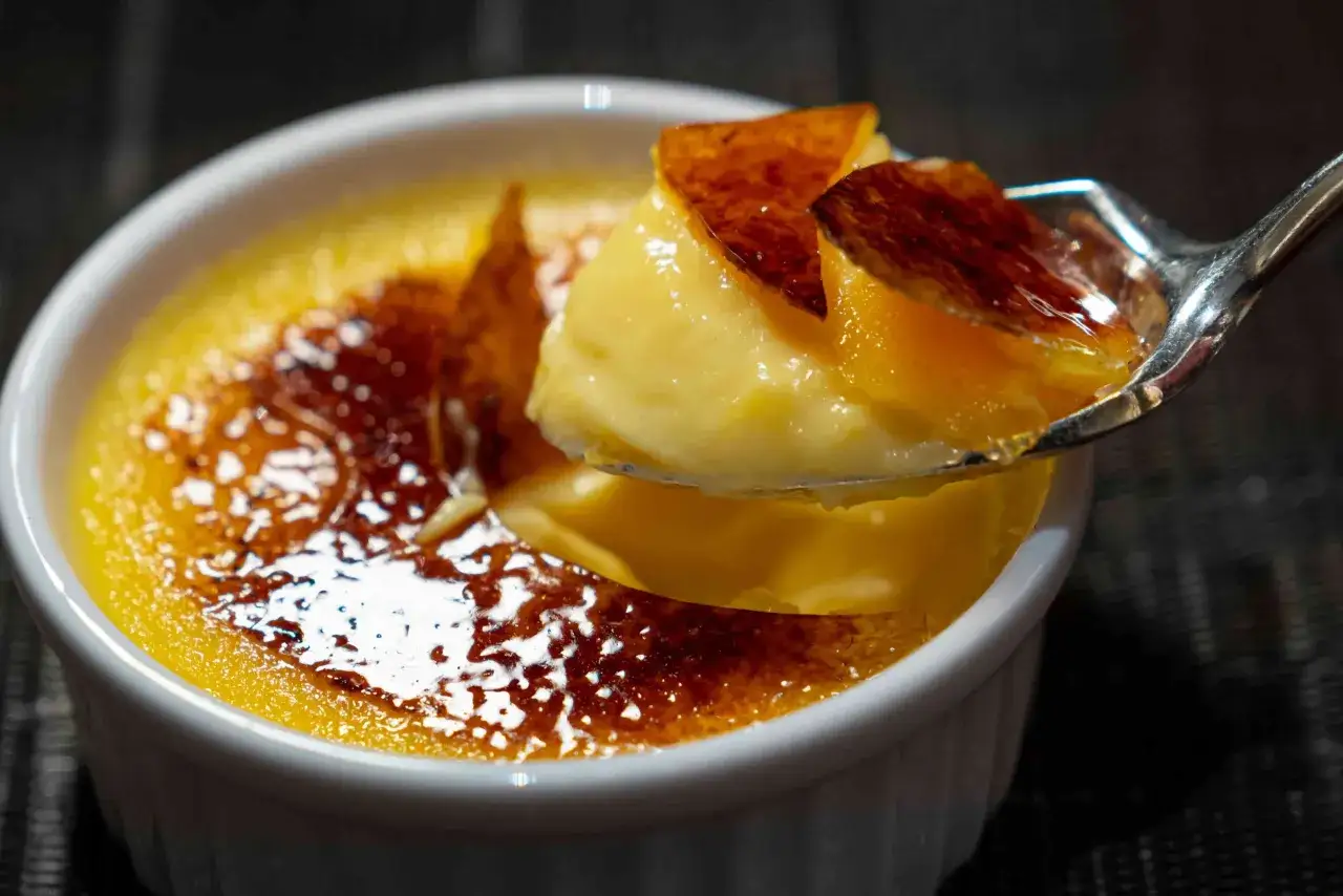 Cr&egrave;me br&ucirc;l&eacute;e avec une cro&ucirc;te caram&eacute;lis&eacute;e craquante. Une cuill&egrave;re en argent pr&eacute;l&egrave;ve une bouch&eacute;e de cette d&eacute;licieuse recette jaune d'oeuf.