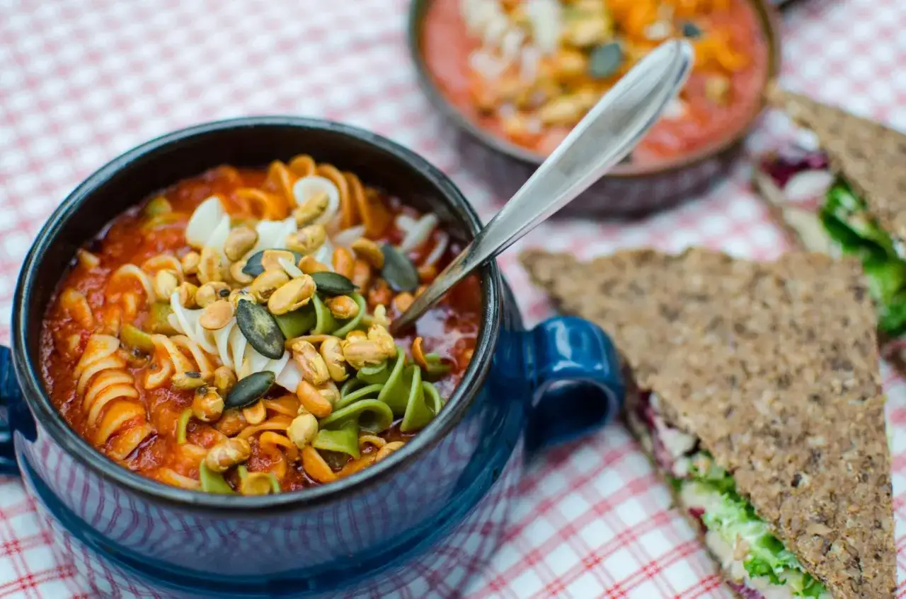 En bl&aring; sk&aring;l med en mustig soppa med pasta, toppad med n&ouml;tter och pumpafr&ouml;n. En sked vilar i sk&aring;len.