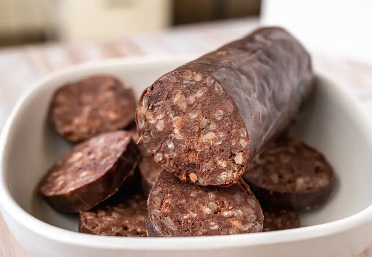 Un plato blanco lleno de rodajas de morcillas, con una morcilla entera apoyada sobre ellas.