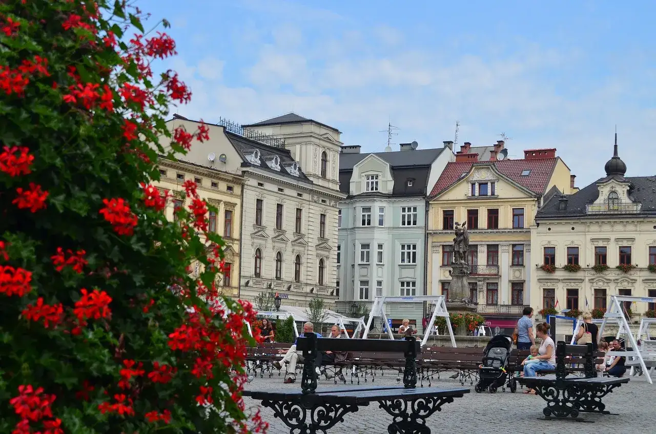Cieszyn atrakcje: kolorowe kamienice, ławki z odpoczywającymi ludźmi i kwitnące czerwone kwiaty na placu miejskim.