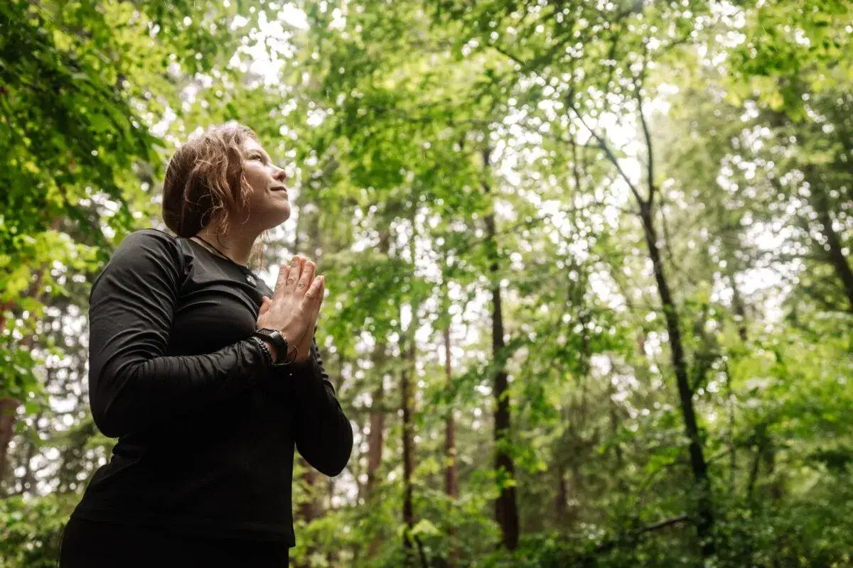 Une femme en pri&egrave;re, profitant d'un moment de shinrin yoku en pleine nature, entour&eacute;e de verdure luxuriante.