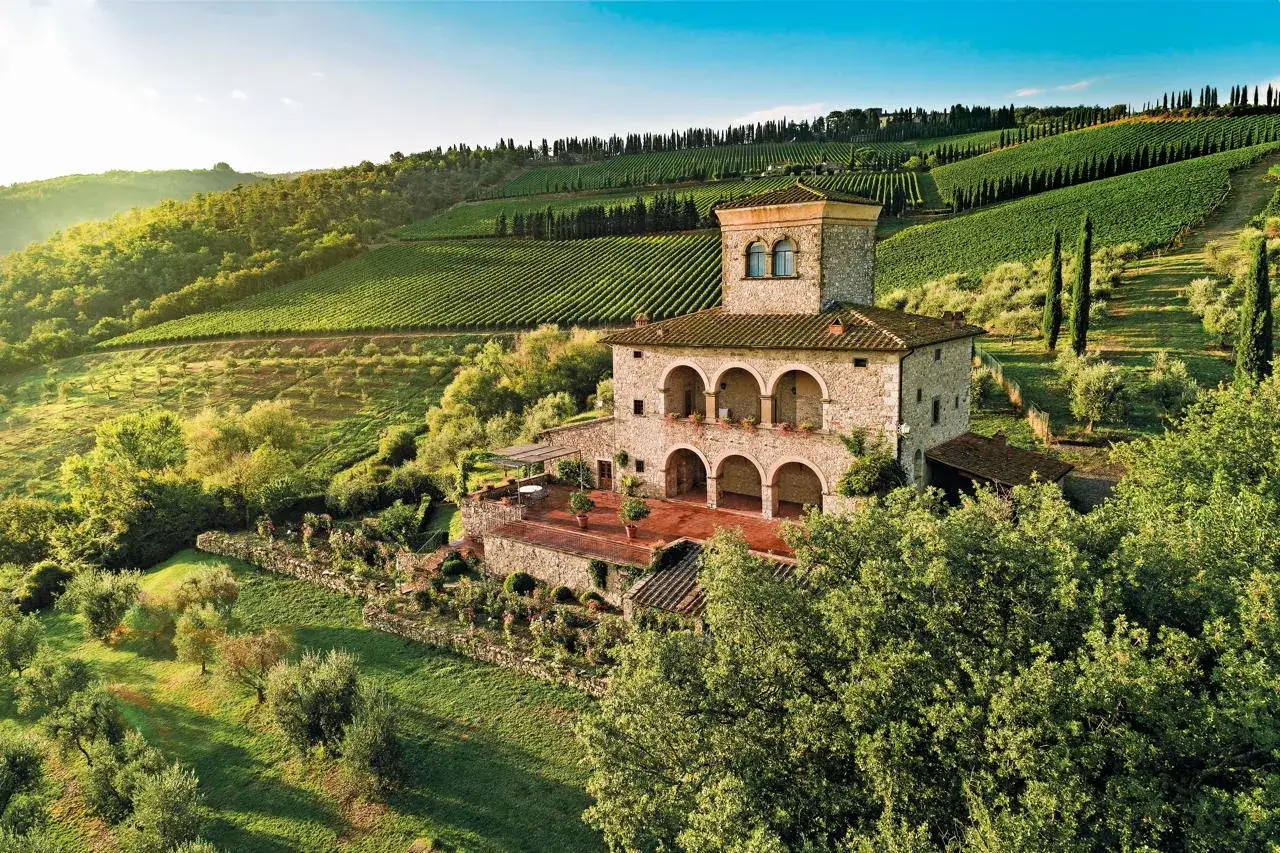 Un casale in pietra con torretta, circondato da vigneti e ulivi, perfetto per un weekend in Toscana.