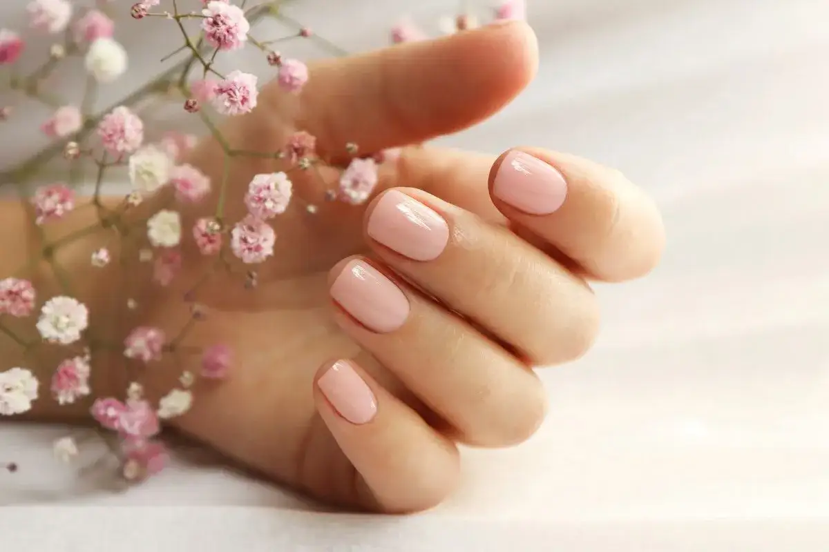 Delikatne, różowe paznokcie na dłoni muśniętej przez gałązkę z drobnymi kwiatkami. Idealna baza kauczukowa dla perfekcyjnego manicure.