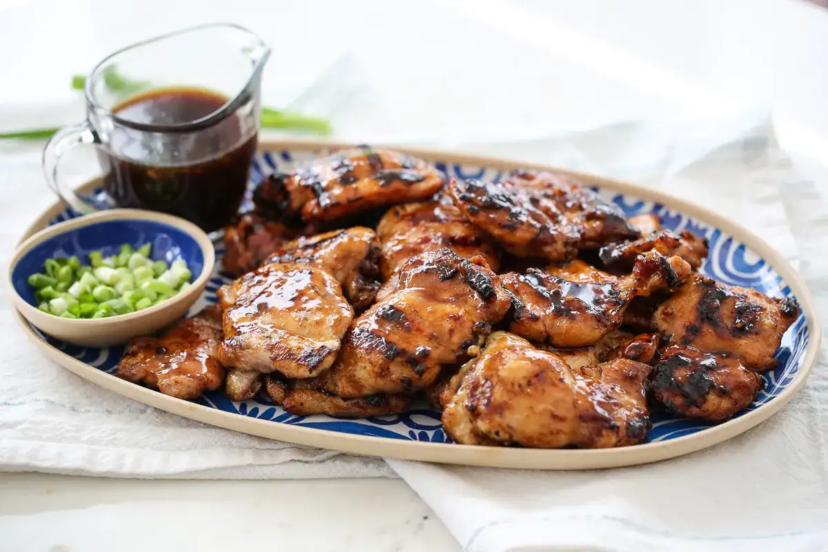 Grilled chicken thighs glistening with teriyaki sauce, served with chopped green onions and a side of extra sauce.