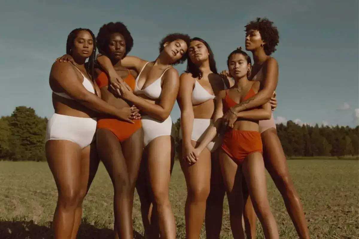 Sześć kobiet o różnych kształtach i odcieniach skóry, w bieliźnie, celebruje body positive na tle natury.