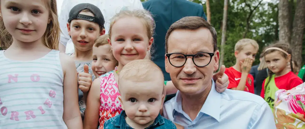 Mateusz Morawiecki z uśmiechem wśród dzieci. Widać radość na twarzach maluchów, które otaczają polityka.