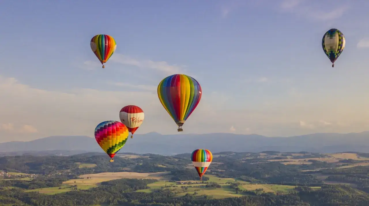 Kolorowe balony unoszą się nad malowniczym krajobrazem. Zastanawiasz się, ile kosztuje lot balonem? To niezapomniane przeżycie!