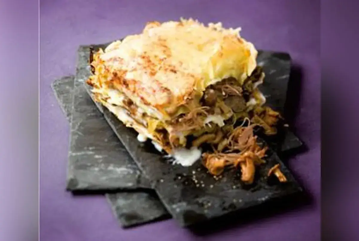 Une g&eacute;n&eacute;reuse lasagne de canard, garnie de champignons, repose sur des ardoises sombres.