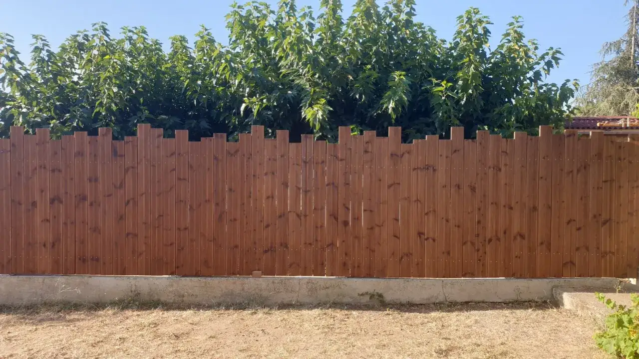 Clôture en bois marron, idéale pour délimiter un jardin. Des arbres verts se dressent derrière.