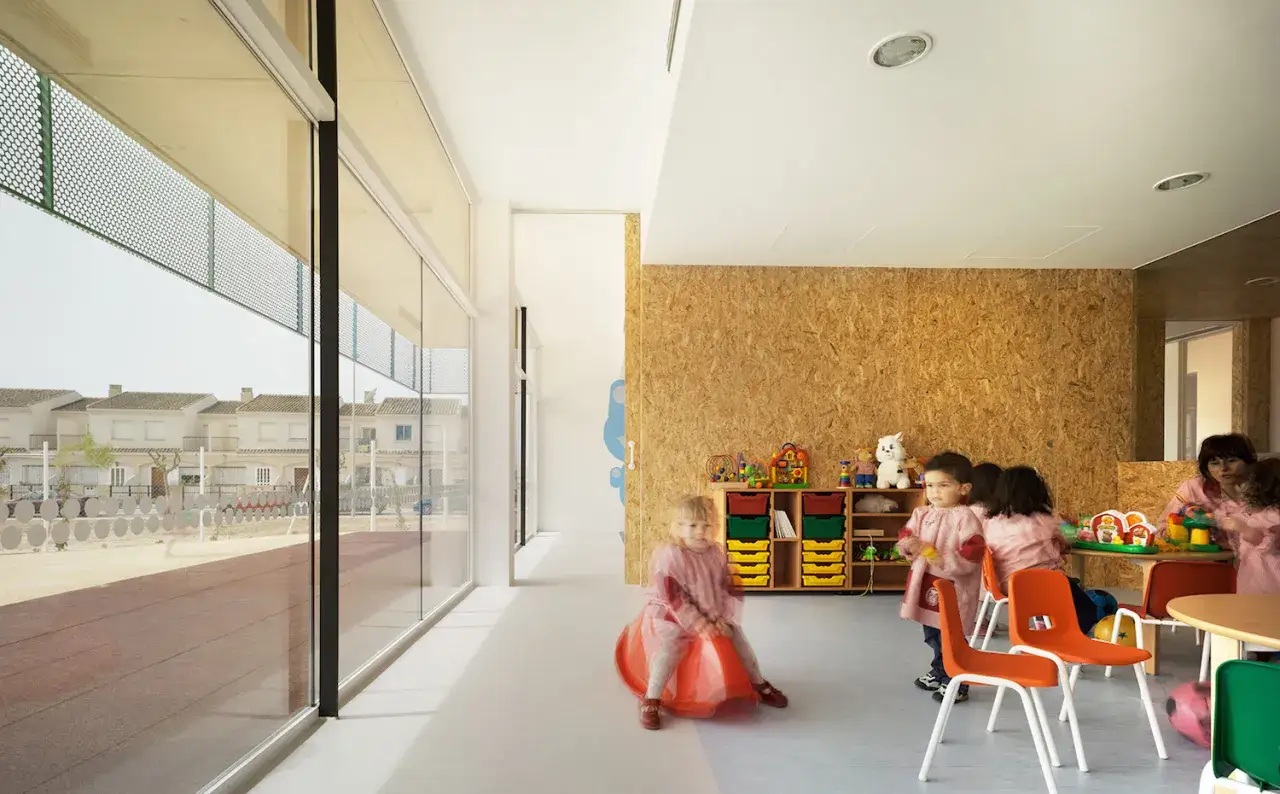 Ni&ntilde;os en el colegio jugando y aprendiendo en un aula luminosa con grandes ventanales.