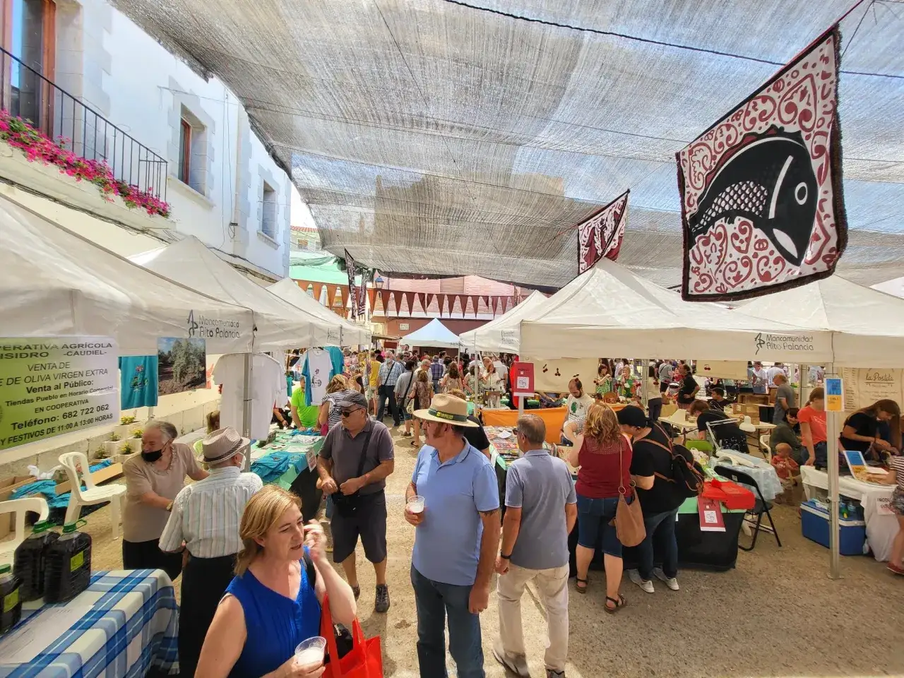 Gente disfrutando en la fiesta de la cereza, con puestos de venta y banderas decorativas.