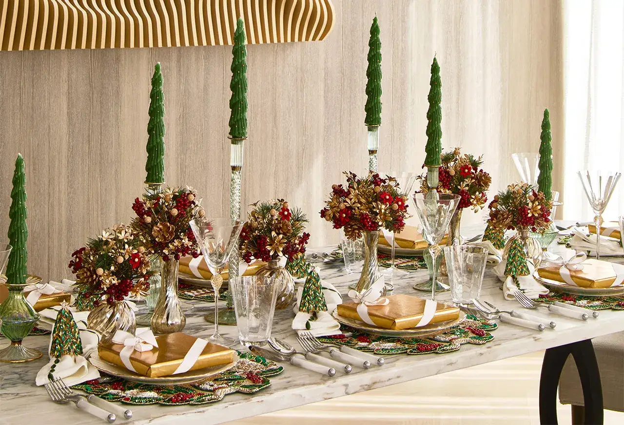 Elegant Christmas tablescape ideas featuring gold-wrapped gifts, festive floral arrangements, and tall, green tree-shaped candles.