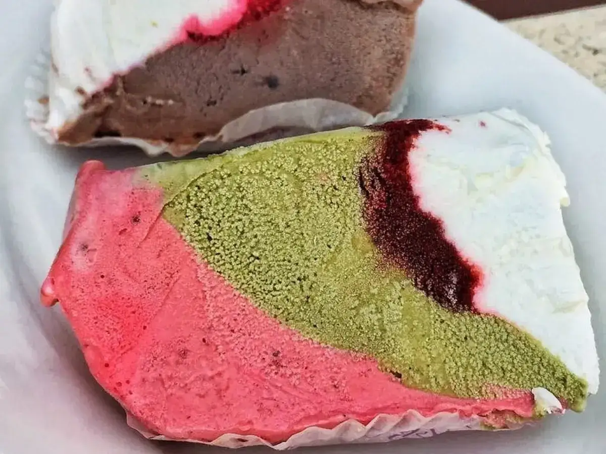Un pezzo duro gelato a strati: rosa, verde pistacchio e bianco con striature rosse. Un altro pezzo di gelato al cioccolato e bianco &egrave; visibile sullo sfondo.