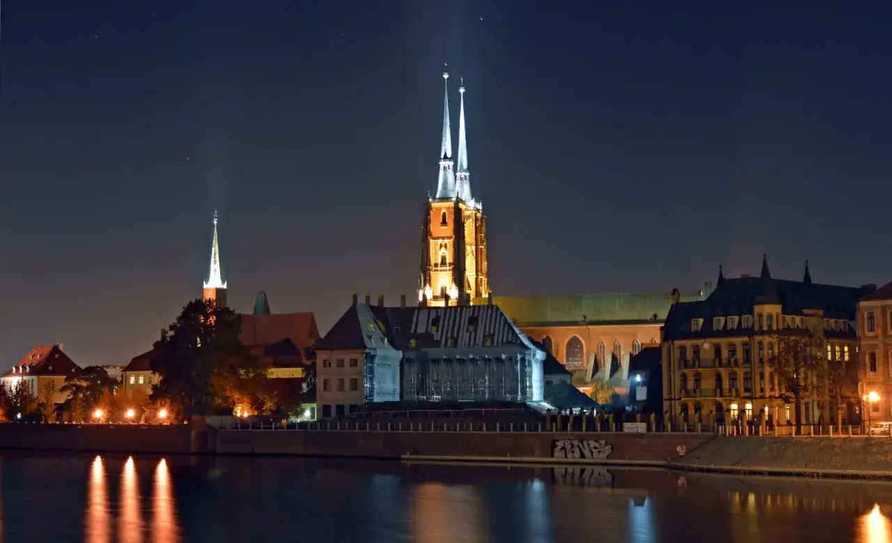 Nocny Wrocław z iluminowanymi wieżami katedry i odbiciem w rzece. Idealne miejsce na wieczorne spacery i odkrywanie wrocławskich atrakcji dla dorosłych.