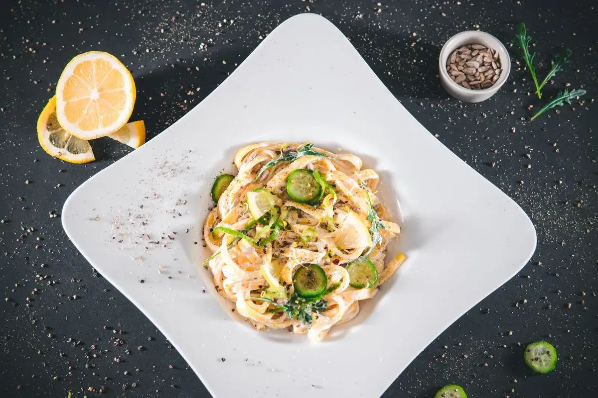Pasta con ricotta cremosa, guarnita con fette di limone, cetrioli e semi di girasole. Un piatto fresco e invitante.