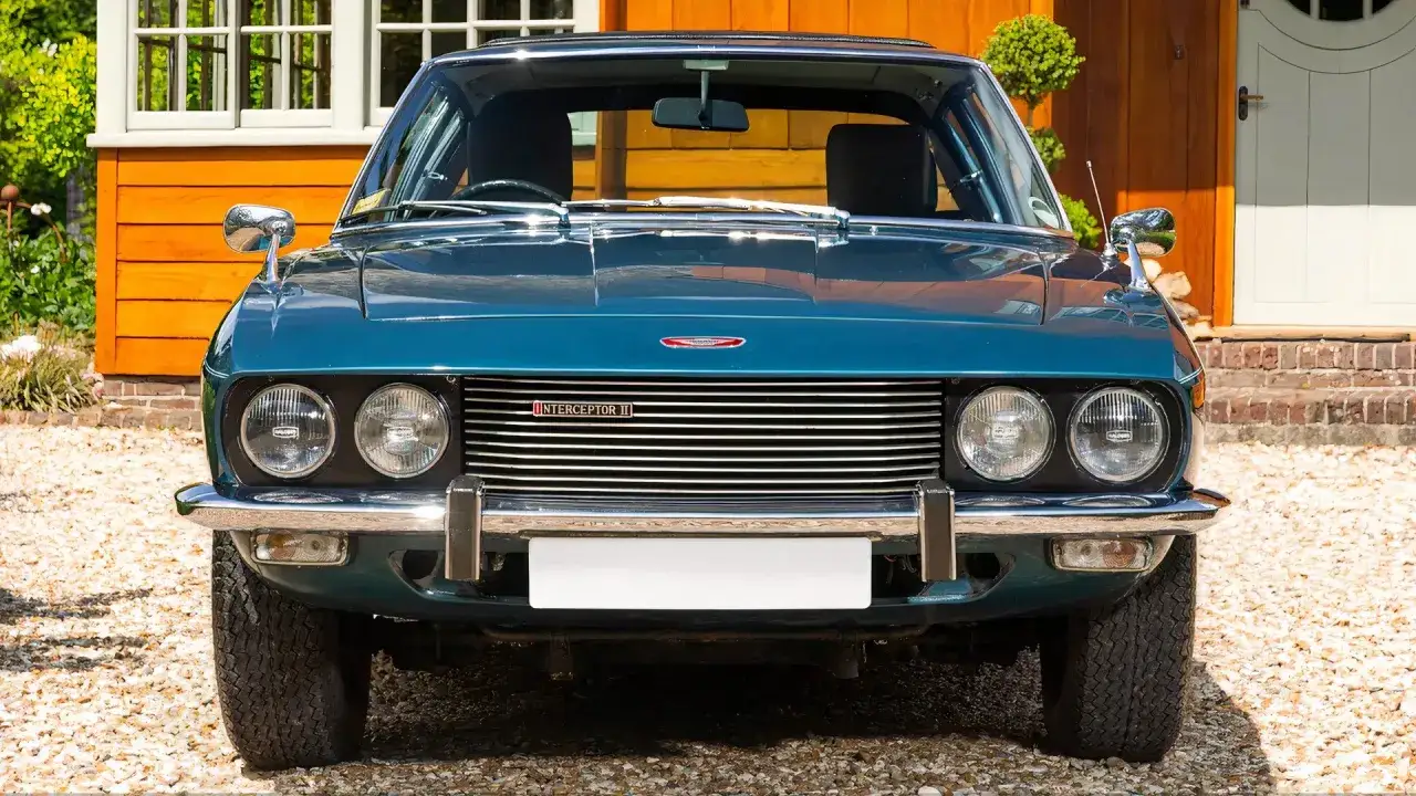 Blå Jensen Interceptor II med kromdetaljer står framför ett trähus.
