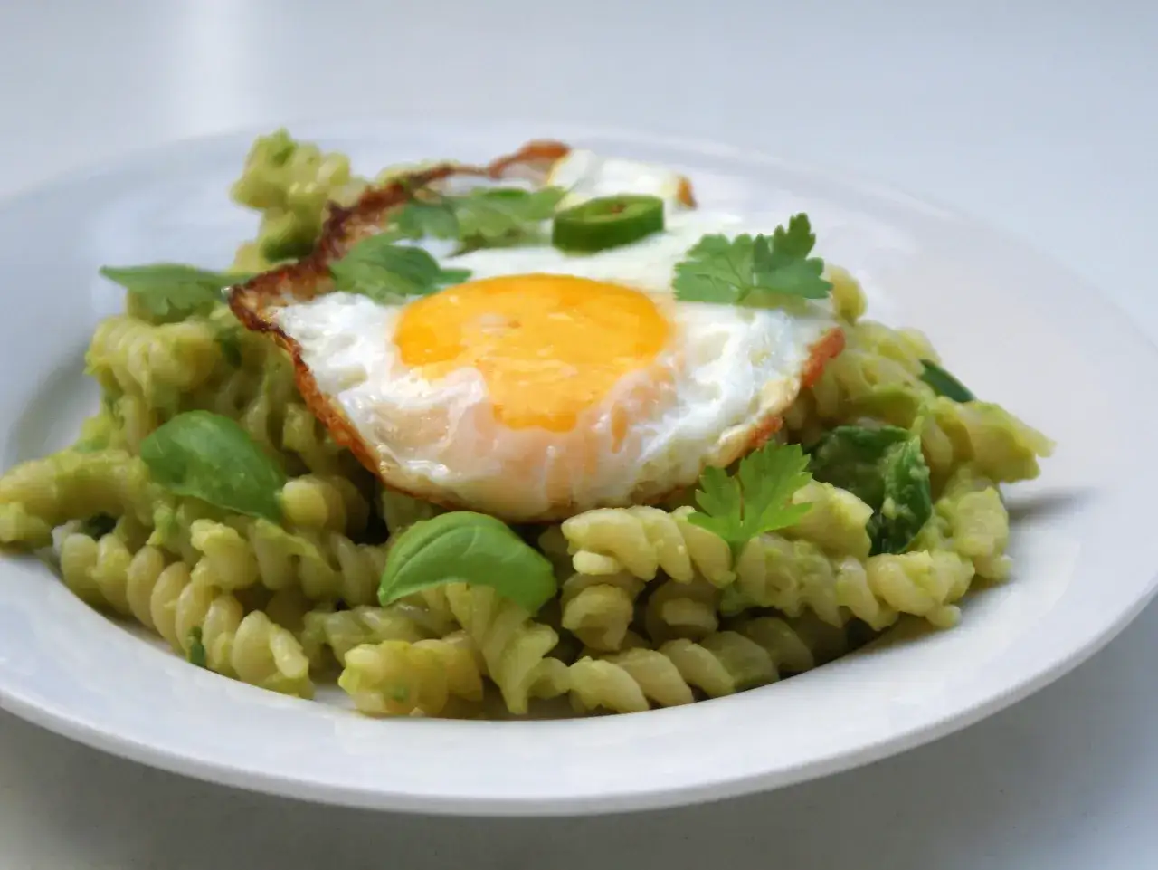 Pyszna pasta z awokado i jajka sadzonego, udekorowana świeżą kolendrą i bazylią.