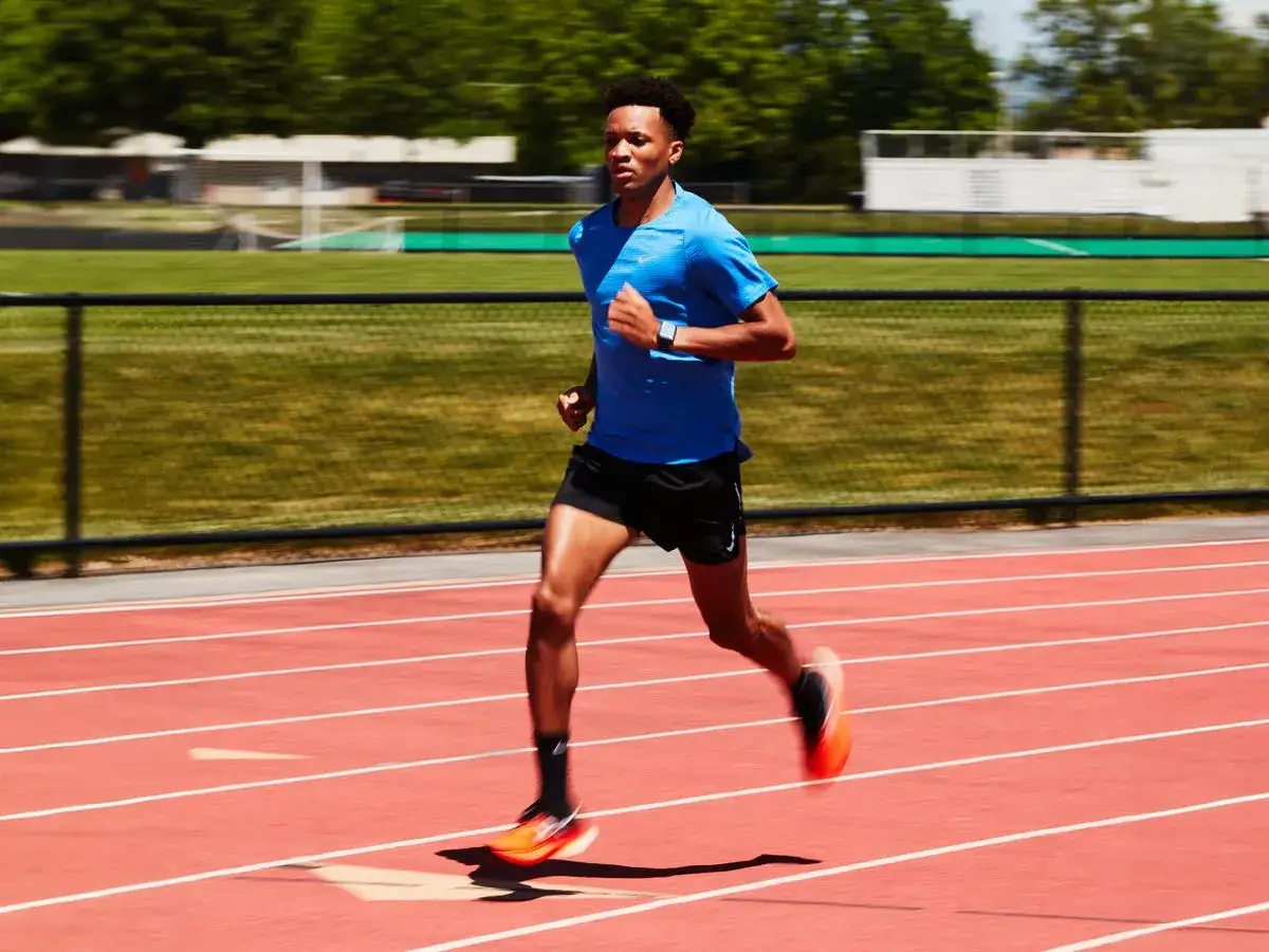 Ein Mann im blauen Shirt und schwarzen Shorts läuft auf einer roten Laufbahn. Sein Tempo steigert sich in einem crescendo lauf.