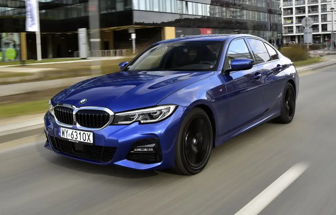 Błękitne BMW 330i G20 mknie ulicą, odbijając nowoczesne budynki w swoich lśniących szybach.