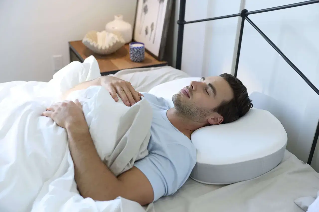 Un homme dort paisiblement sur un oreiller ergonomique, espérant soulager ses douleurs lombaires et cervicales.