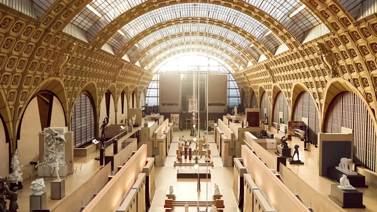 Interior del museo d'Orsay, con esculturas y arcos dorados bajo un techo de cristal.