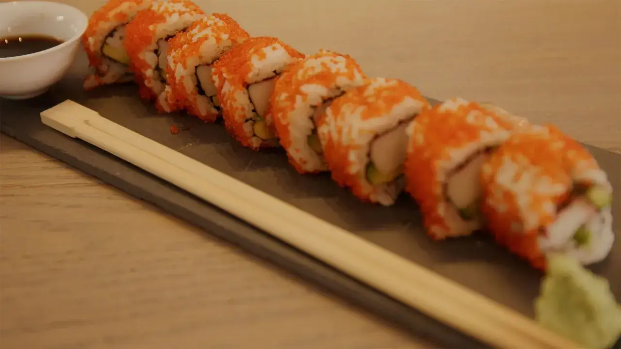 Rząd roladek california sushi z pomarańczową ikrą, pałeczki i sos sojowy.