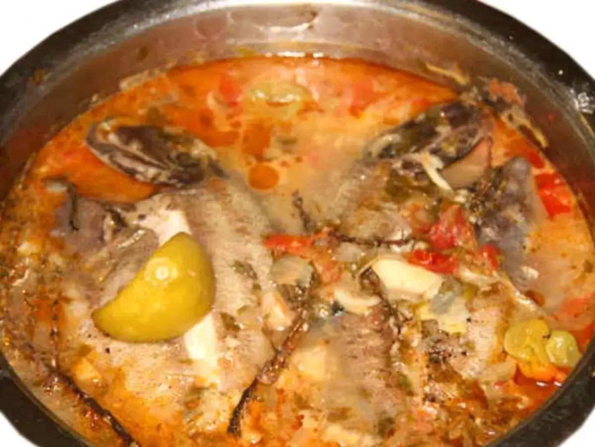 Un fumetto di pesce in umido, con pomodoro, limone e spezie, in una pentola.