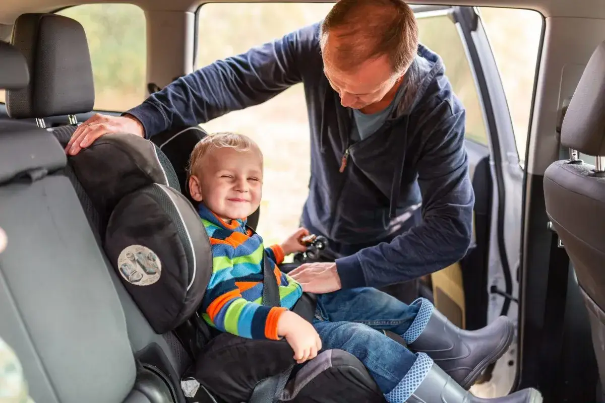 Padre ajusta el sistema de retención para su hijo, asegurando su seguridad en el asiento del coche.