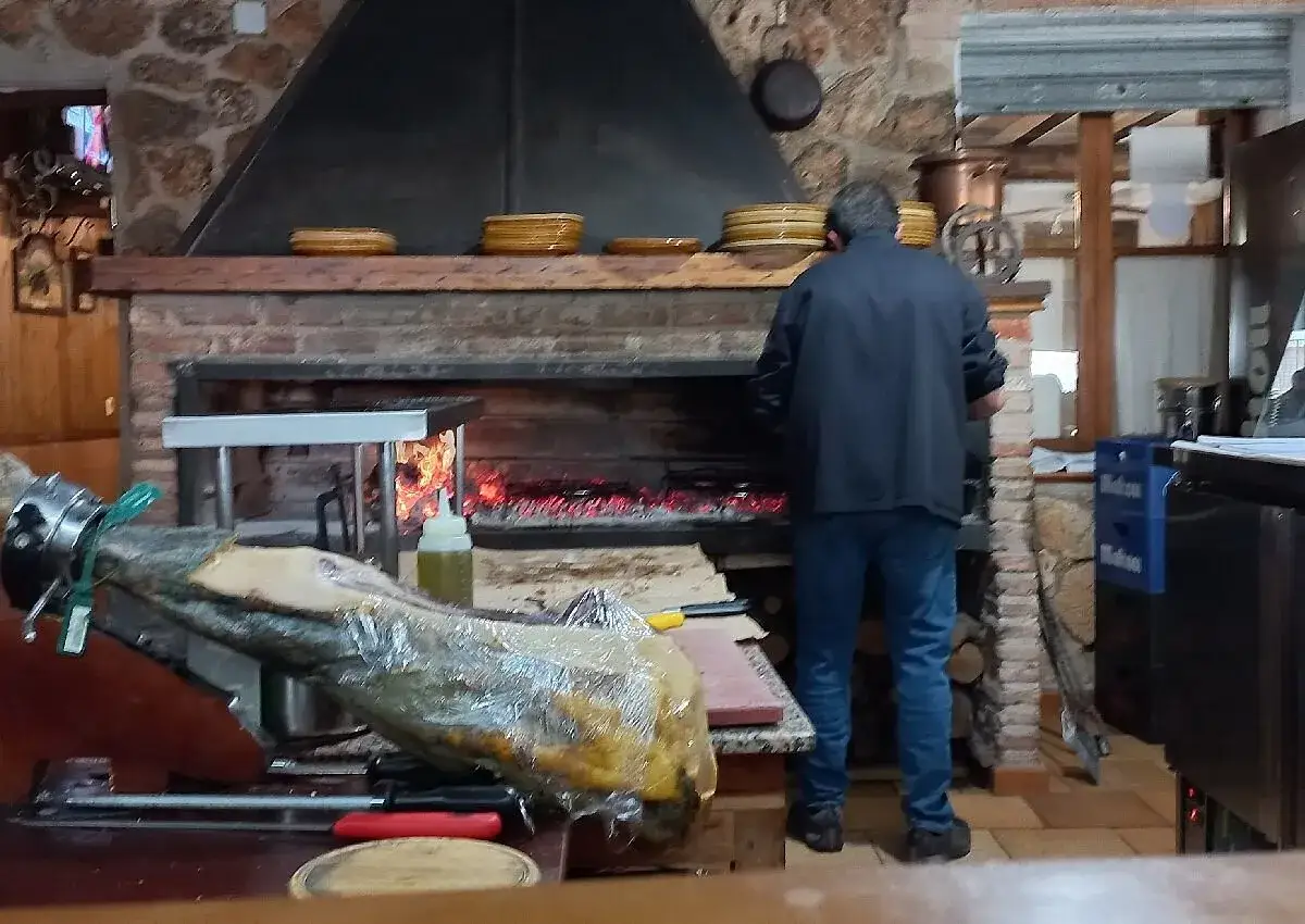 Un hombre trabaja en la cocina del restaurante Emilio Riobar, cerca de un jamón y un horno de leña.