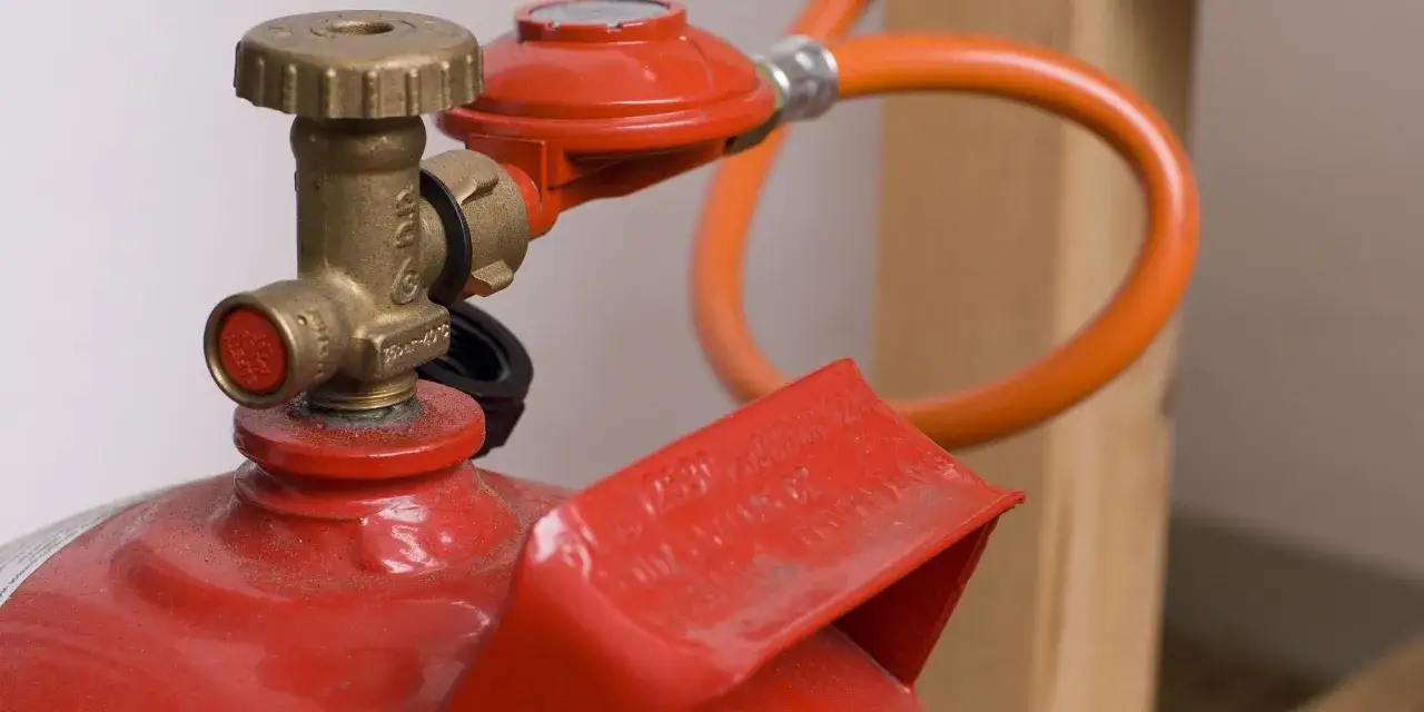 Détail d'une bouteille de gaz propane rouge avec détendeur et tuyau orange, conforme à la norme installation gaz propane bouteille.